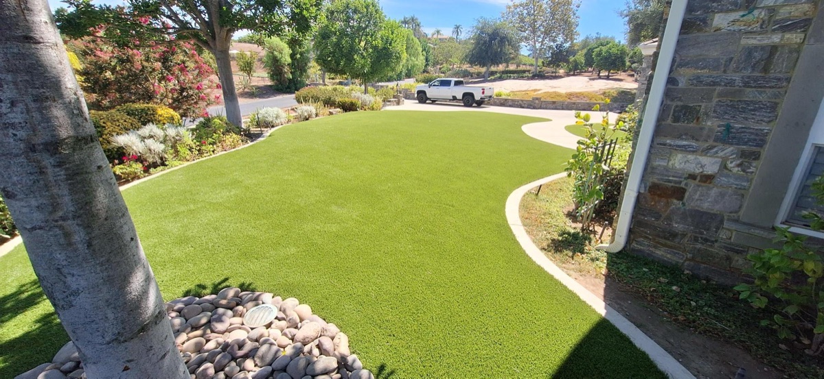 Front yard artificial turf lawn with stone facade and curved concrete border in North County San Diego